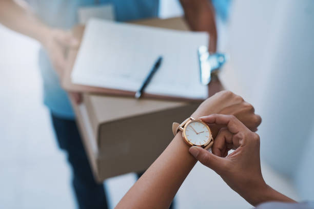 Cropped shot of an unidentifiable businesswoman checking the time on her watch as the courier arrives with a delivery